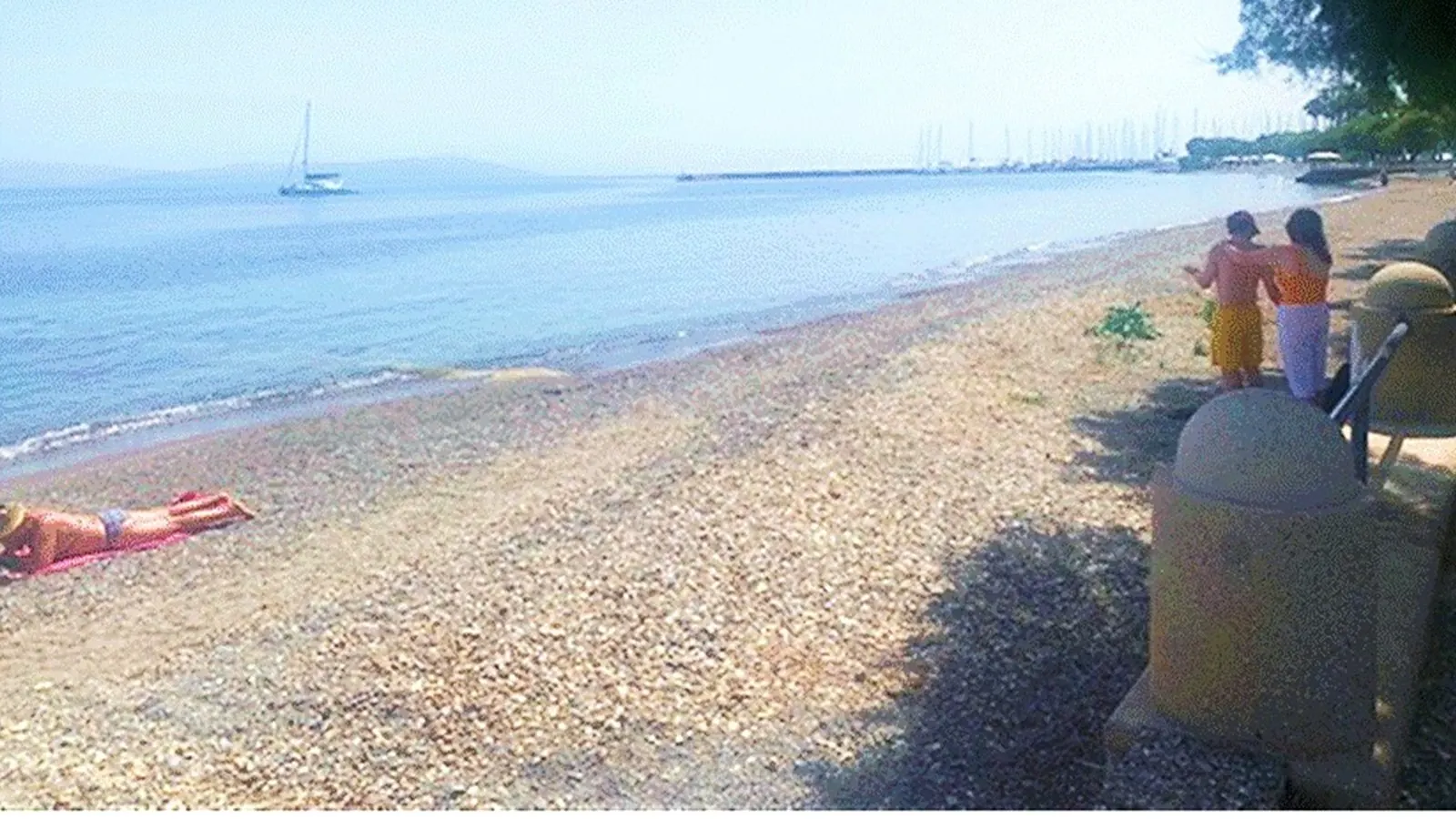 Summer use of the shingle beach on Kos, Dodecanese, with moored boats offshore and concrete structures along the shoreline